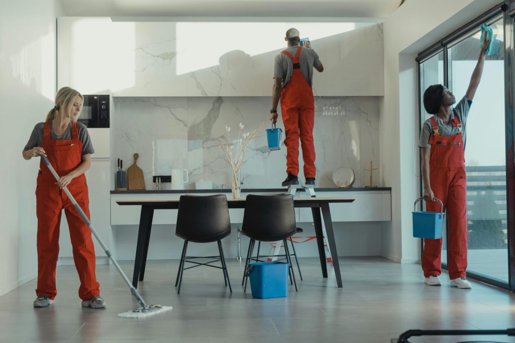 Group of cleaners in red uniforms mopping and wiping glass in a modern room.